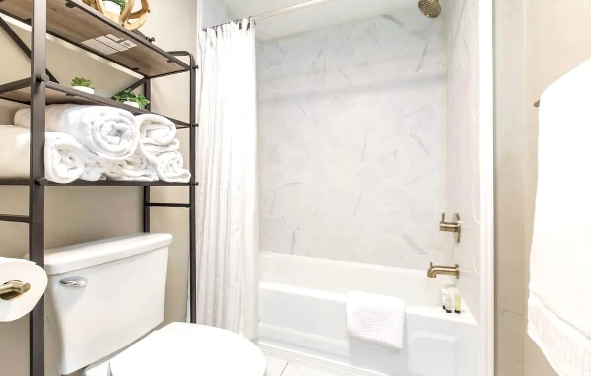 A refreshing bathroom with a modern shelving unit stocked with fluffy white towels, a bathtub with a shower, and a simple shower curtain. The space is clean, serene, and designed for relaxation and convenience.