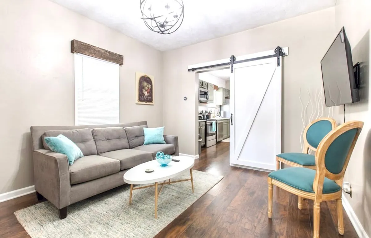 A bright yet cozy living area with a comfortable sofa, coffee table, sliding door, wall art, and TV. Sunlight pours in, suggesting easy access to the outdoors and a space to relax after exploring.