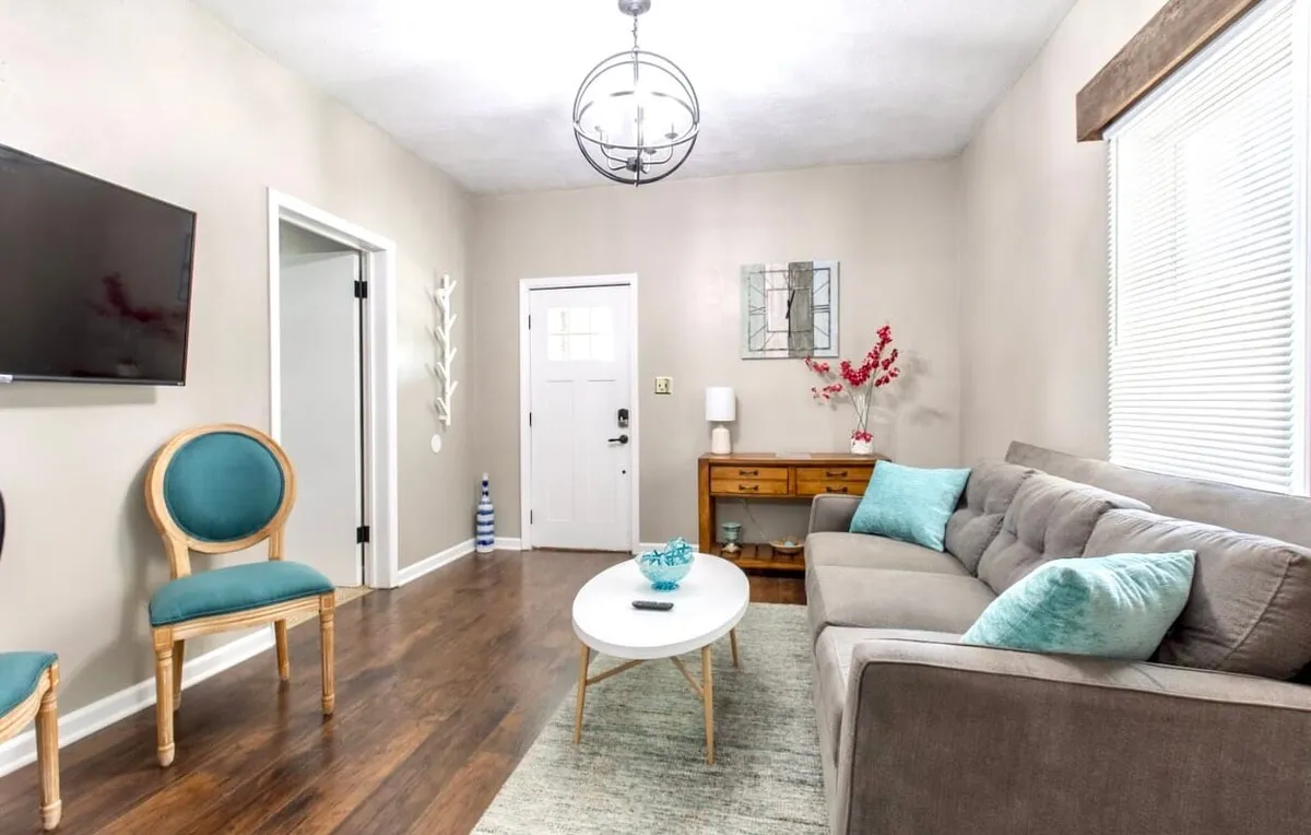This image presents a warm, welcoming living space with a sofa, coffee table, decorative chair, and striking wall art. It suggests a space designed for group activities like game nights, casual conversations, and relaxed TV watching, reinforcing the inclusive and cheerful ambiance described in the section.