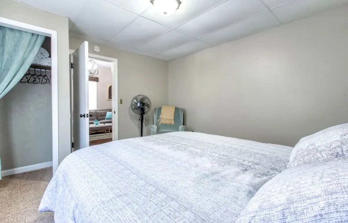 A restful bedroom styled with patterned bedding, a soft blue accent chair, and a ceiling fan. The decor is tranquil and inviting, encouraging relaxation and quiet activities like reading or napping.